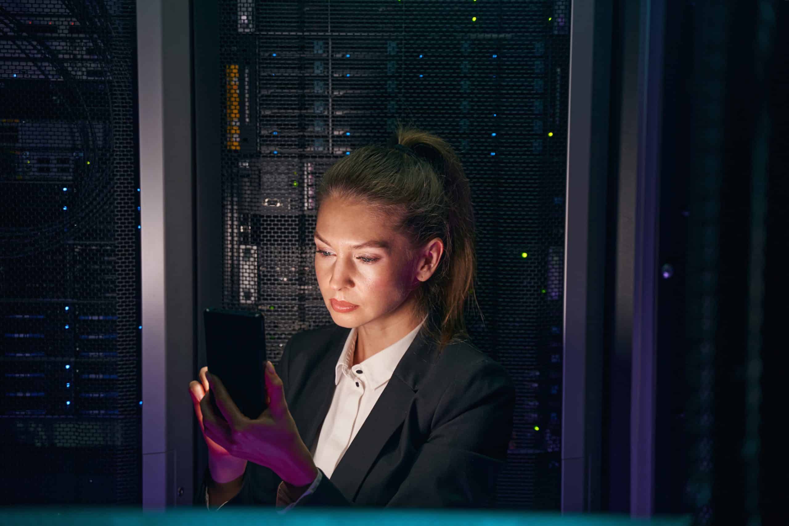 Photo of confident businesswoman using cellphone while working with supercomputer in data center server room